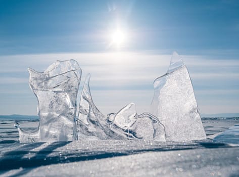 The serene landscape of Lake Baikal in winter, featuring captivating, transparent ice formations under a bright sky with the sun shining brightly above.