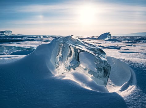 A stunning block of ice sits on the snow, shimmering in the early morning light of a winter sunrise on Lake Baikal, Siberia.