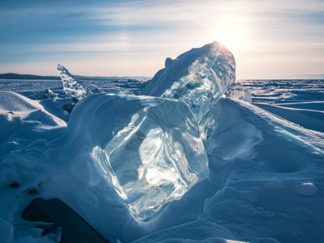 The serene landscape of Lake Baikal in winter, featuring captivating, transparent ice formations under a bright sky with the sun shining brightly above.
