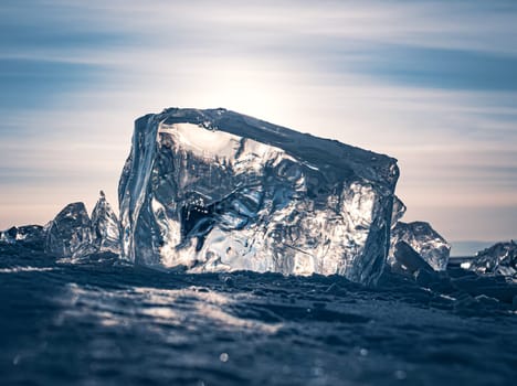 A stunning block of ice sits on the snow, shimmering in the early morning light of a winter sunrise on Lake Baikal, Siberia.