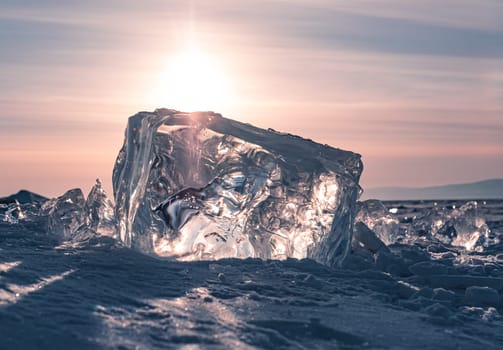 A stunning block of ice sits on the snow, shimmering in the early morning light of a winter sunrise on Lake Baikal, Siberia.