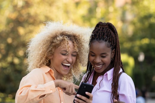 Two multiethnic girls laughing while checking something funny in the smartphone.