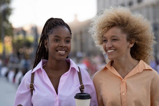 two multiracial girls friends together taking a break and holding a coffee cup outdoors.