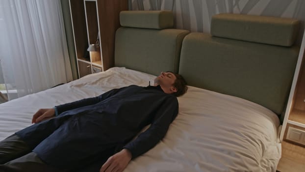 Young man lying dressed in clothes on a bed unconscious or sleeping exhausted. Stock clip. Caucasian male lying on bed in a room with eyes closed