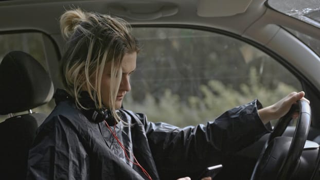 Young man worries and looks at phone in car. Stock. Man looks at phone during nervous breakdown in car. Man is nervous sitting in car and looking at phone.