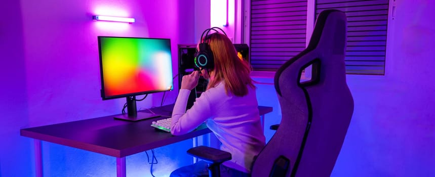 Asian woman gamer wearing gaming headphones holding joystick console to play video game and streaming online on computer PC neon light at home, tournament player E-Sport concept