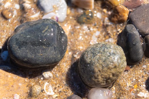 A close-up view capturing two stones resting atop a bed of beach sand and gently lapped by the coastal waters