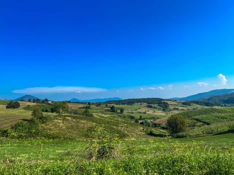 Han Kola, Bosnia and Herzegovina, August 23, 2023: View of small hills and larger mountains with a small field and a house