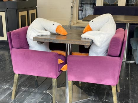 Two goose toys sitting on chairs at the restaurant table