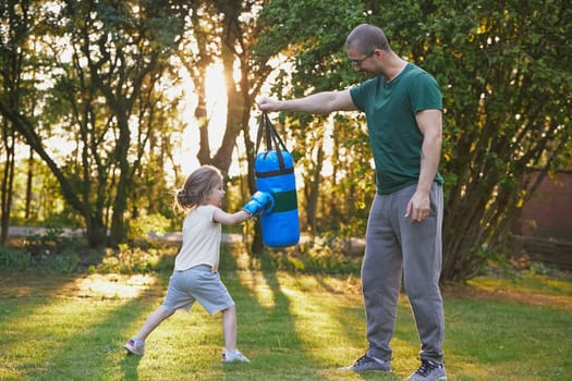 Father training his daughter to box in the backyard at sunset.