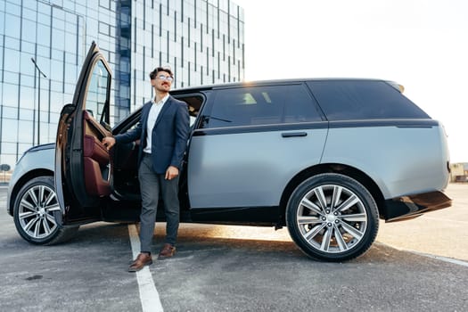 Young handsome businessman in a suit comes out of the luxury car close up