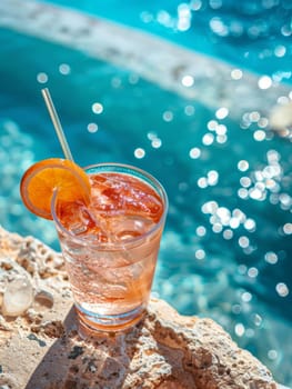 A glass of pink drink with ice cubes in it is sitting on a ledge by a pool. The drink is a refreshing beverage to enjoy on a hot day by the water