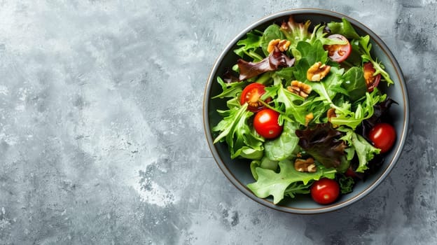 An overhead view of a nutritious bowl of salad with leafy greens, cherry tomatoes, and walnuts on a grey background. Banner with copy space.