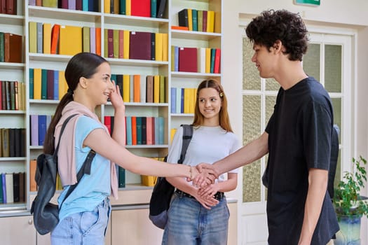 Meeting of classmates in high school library, teenagers students shaking hands and greeting them. Friendship, communication, adolescence, education concept