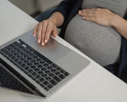 A pregnant woman works on a laptop in the office. Close-up of the tummy