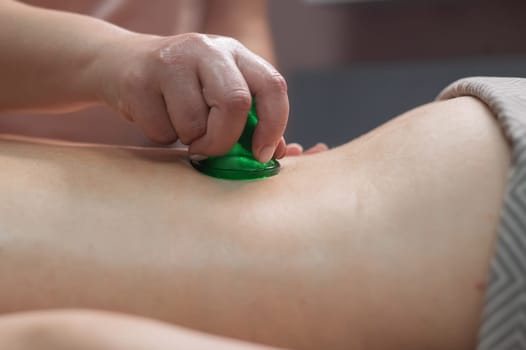 A woman undergoes an anti-cellulite massage procedure using a vacuum jar. Close-up of the lower back