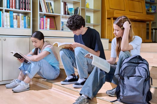 Teenage students sitting in college high school library reading books. Education, training, adolescence and youth concept