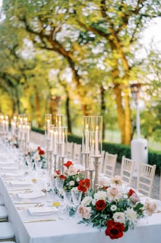 Glowing candles on a festive table among flowers in a green park. High quality photo