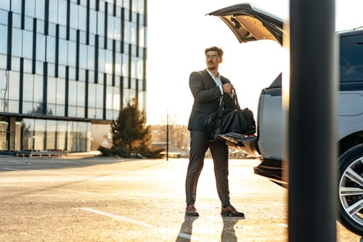 Successful businessman taking luggage from the car trunk outdoors