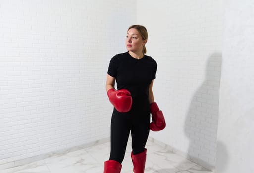 Portrait of a beautiful confident Caucasian woman in sportswear and red boxing equipment, looking aside, practicing box and kickbox, isolated over white background. Copy advertising space for text