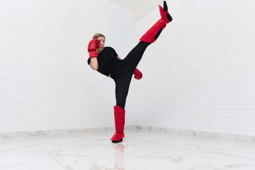 Full length authentic portrait of young European sporty woman in sports equipment, doing boxing exercises. Determined female kick boxer kicking, exercising isolated over white background.