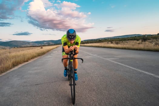 Triathlete riding his bicycle during sunset, preparing for a marathon. The warm colors of the sky provide a beautiful backdrop for his determined and focused effort