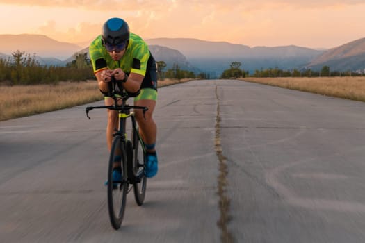 Triathlete riding his bicycle during sunset, preparing for a marathon. The warm colors of the sky provide a beautiful backdrop for his determined and focused effort