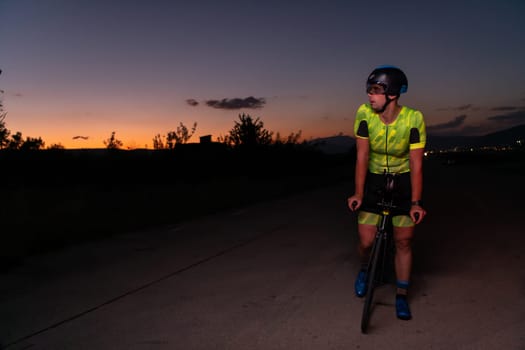 A triathlete rides his bike in the darkness of night, pushing himself to prepare for a marathon. The contrast between the darkness and the light of his bike creates a sense of drama and highlights the athlete's determination and perseverance