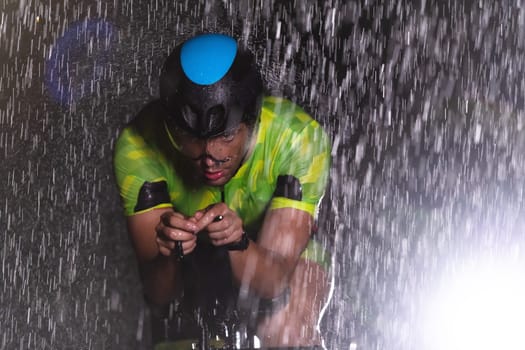 A triathlete braving the rain as he cycles through the night, preparing himself for the upcoming marathon. The blurred raindrops in the foreground and the dark, moody atmosphere in the background add to the sense of determination and grit shown by the athlete