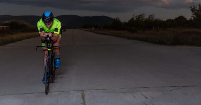 A triathlete rides his bike in the darkness of night, pushing himself to prepare for a marathon. The contrast between the darkness and the light of his bike creates a sense of drama and highlights the athlete's determination and perseverance