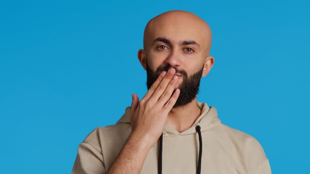 Lovely sweet person blowing air kisses on camera, dping romantic gesture and being flirty over blue background. Middle eastern guy sending a kiss to express his honest feelings. Camera 2.