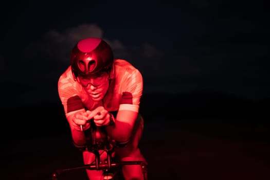 A triathlete rides his bike in the darkness of night, pushing himself to prepare for a marathon. The contrast between the darkness and the light of his bike creates a sense of drama and highlights the athlete's determination and perseverance