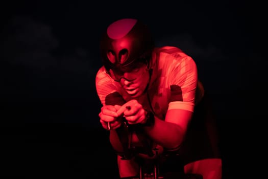 A triathlete rides his bike in the darkness of night, pushing himself to prepare for a marathon. The contrast between the darkness and the light of his bike creates a sense of drama and highlights the athlete's determination and perseverance