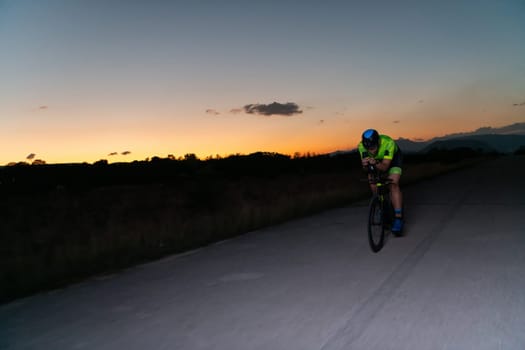 A triathlete rides his bike in the darkness of night, pushing himself to prepare for a marathon. The contrast between the darkness and the light of his bike creates a sense of drama and highlights the athlete's determination and perseverance