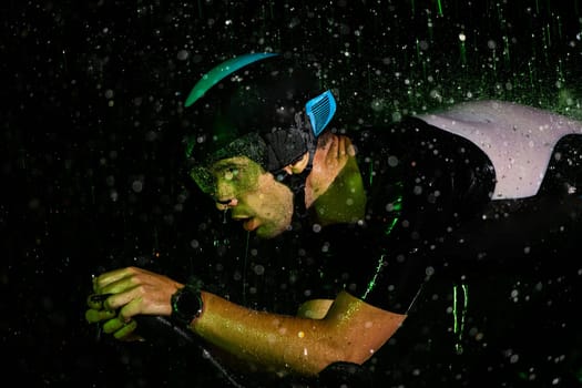 A triathlete braving the rain as he cycles through the night, preparing himself for the upcoming marathon. The blurred raindrops in the foreground and the dark, moody atmosphere in the background add to the sense of determination and grit shown by the athlete