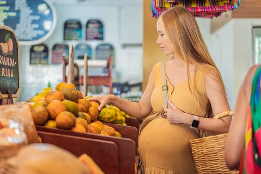 In a grocery store, a pregnant woman stands by a fruit stand, surrounded by various natural foods. She is in a public space where the local market offers whole foods for trade Pregnant woman buying organic vegetables and fruits at Mexican style farmers market