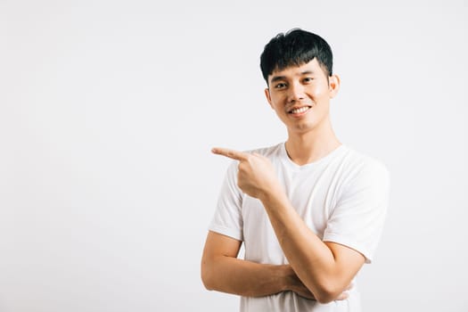 Portrait of a confident Asian young man smiling and pointing his finger towards empty space. Studio shot isolated on white background, with copy space for your product or message.