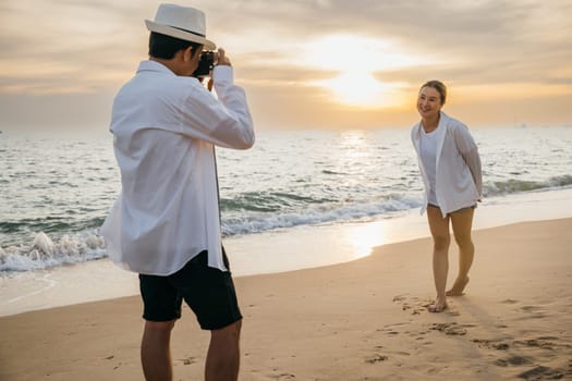 A couple in white attire celebrates love at sunrise by sea with boyfriend skillfully taking photos of his girlfriend. beach becomes canvas for their romance creating beautiful memories together.