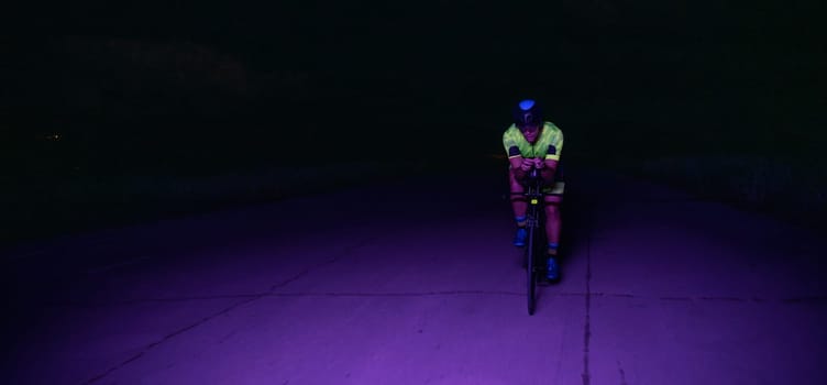 A triathlete rides his bike in the darkness of night, pushing himself to prepare for a marathon. The contrast between the darkness and the light of his bike creates a sense of drama and highlights the athlete's determination and perseverance