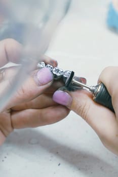 Close-up of a dental technician examining a metal prosthesis for a tooth, part of the manufacturing process in dentistry.