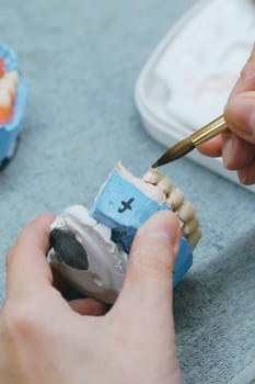 Close-up view of a dental technicians hands holding a toothbrush, focusing on manufacturing prosthesis using dental materials and tools for oral care. Vertical photo.