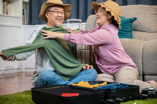 Asian couple old senior marry retired couple smiling prepare luggage suitcase arranging for travel, Romantic mature retired packing clothes travel bag suitcase together on floor at home for holiday