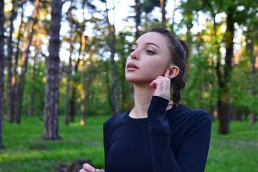 Portrait of a young woman in a forest listening to music on wireless headphones.