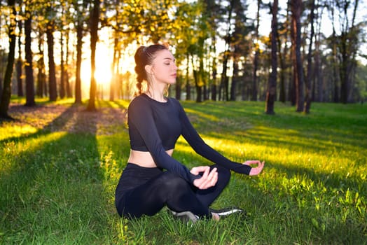 A woman is meditating in a forest at sunset, engaging in yoga and mindfulness, surrounded by the beauty of nature