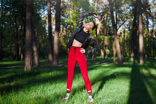 Active woman in red sportswear stretches before a run in a sunny green park