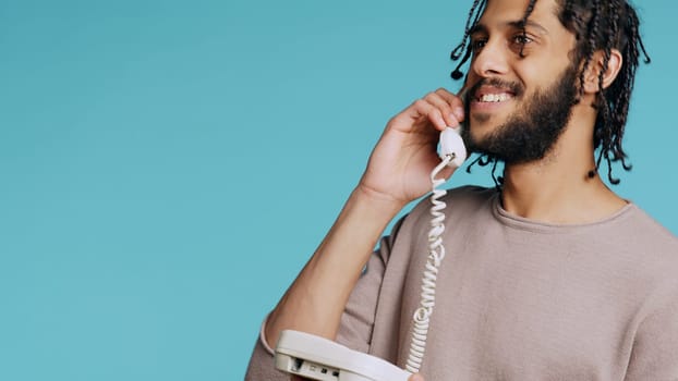 Middle Eastern man chatting with best friend over telephone call. Upbeat person talking with mate using landline phone, isolated over studio background, camera B close up