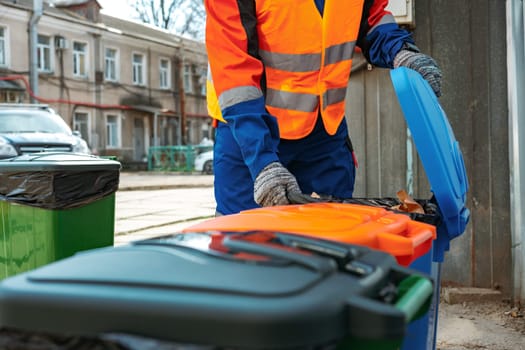 Male janitor in uniform cleans a trash can in the street close up