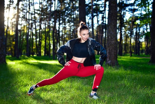 Woman in red workout pants stretching outdoors in a forest. Exercising in nature.