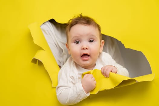 Cute Caucasian baby sticking out of a hole in a paper yellow background