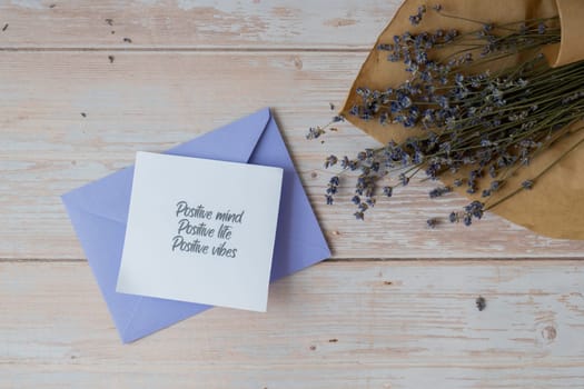 Female hands taking paper card note with text POSITIVE MIND LIFE VIBES from violet envelope. Lavender flower. Top view, flat lay. Concept of mental spiritual health self care wellbeing mindfulness